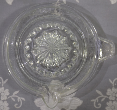Crown on thumb grip and vine pattern around  clear glass juicer top view